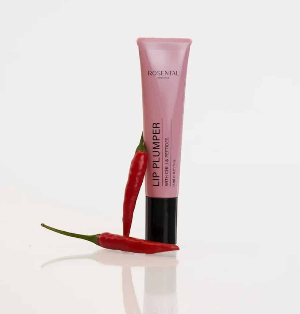 Rosental Lip Plumper Tube neben zwei roten Chilischoten, um die Inhaltsstoffe Chili und Peptide zu symbolisieren.